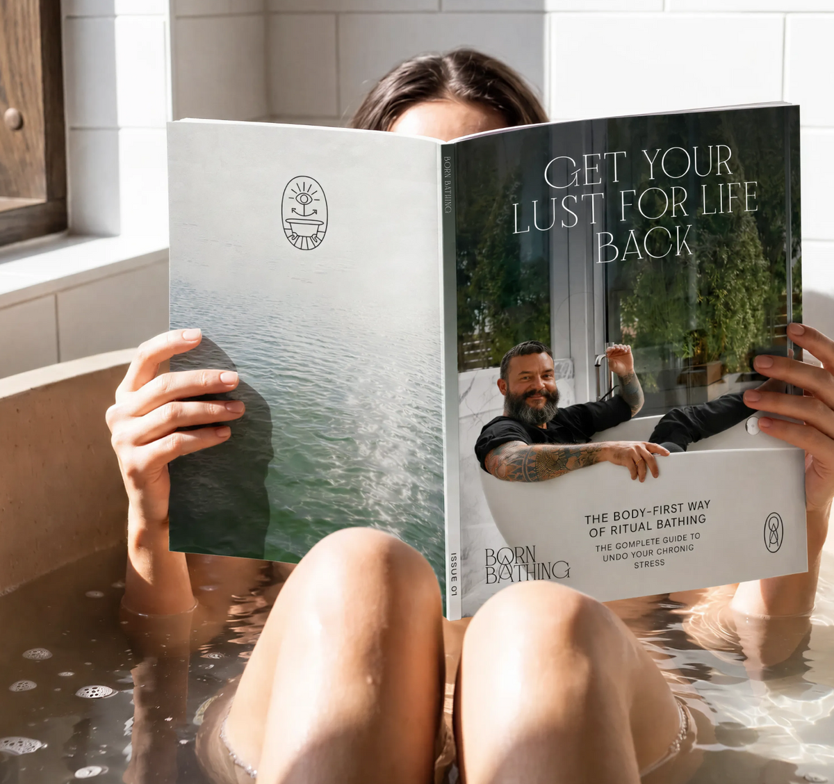 A person sitting in a bubble bath holds a printed booklet or magazine open in front of their face. The booklet cover shows a large photo of a man in a bathtub with the text 'GET YOUR LUST FOR LIFE BACK' and branding for 'Born Bathing'.